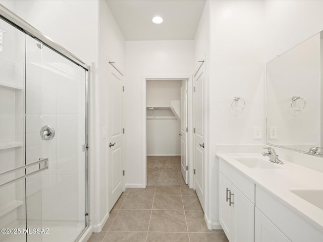 bathroom with a sink, a shower stall, tile patterned flooring, double vanity, and a spacious closet