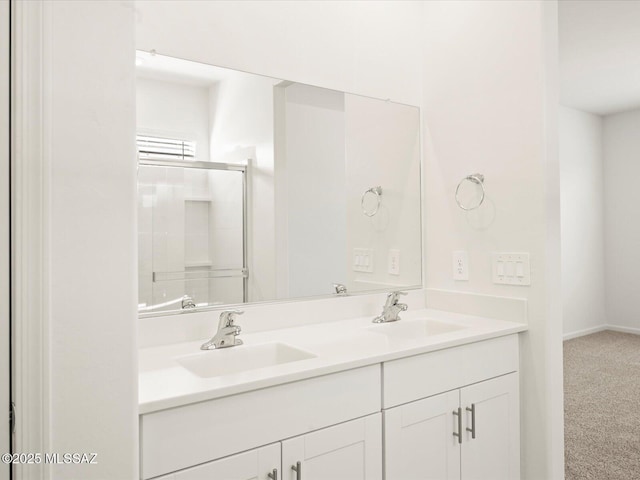 bathroom with double vanity, baseboards, a shower with shower door, and a sink