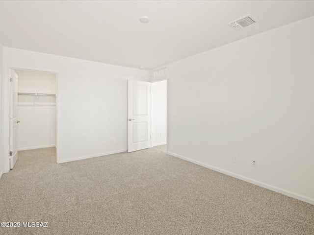 unfurnished bedroom featuring visible vents, a walk in closet, baseboards, light colored carpet, and a closet