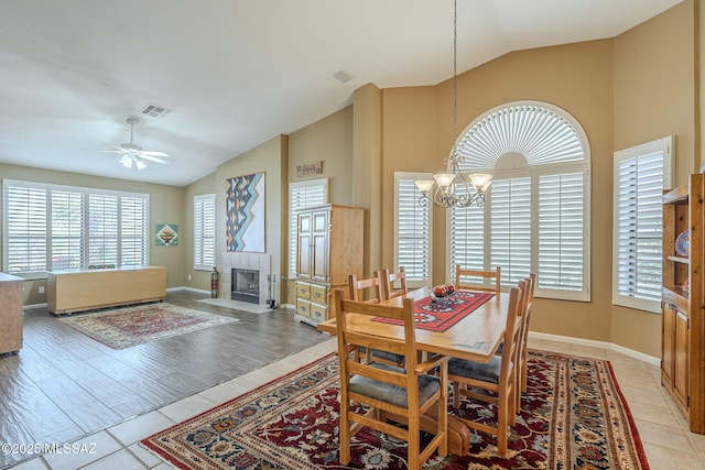 dining area with visible vents, a tiled fireplace, ceiling fan with notable chandelier, vaulted ceiling, and light tile patterned flooring