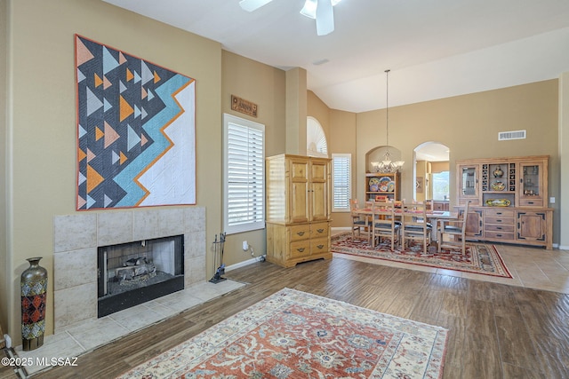 living area with visible vents, wood finished floors, high vaulted ceiling, a tile fireplace, and baseboards