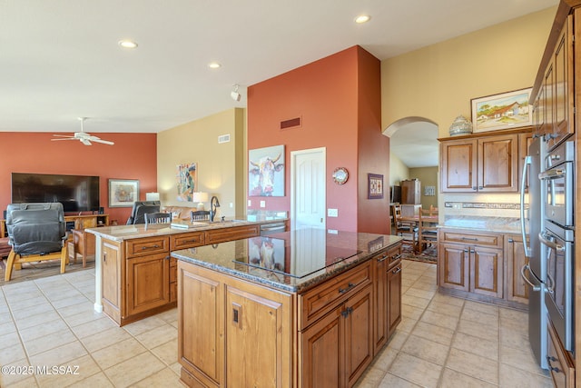 kitchen with arched walkways, lofted ceiling, black electric stovetop, a kitchen island, and dark stone counters