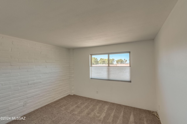 carpeted empty room featuring brick wall