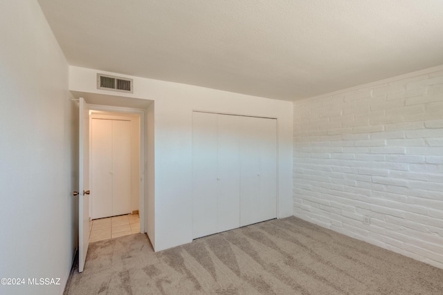 unfurnished bedroom featuring a closet, brick wall, and light carpet