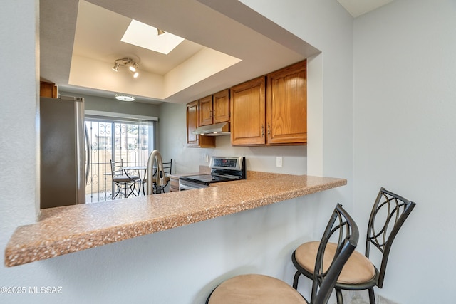 kitchen with a raised ceiling, a breakfast bar area, a peninsula, stainless steel appliances, and light countertops