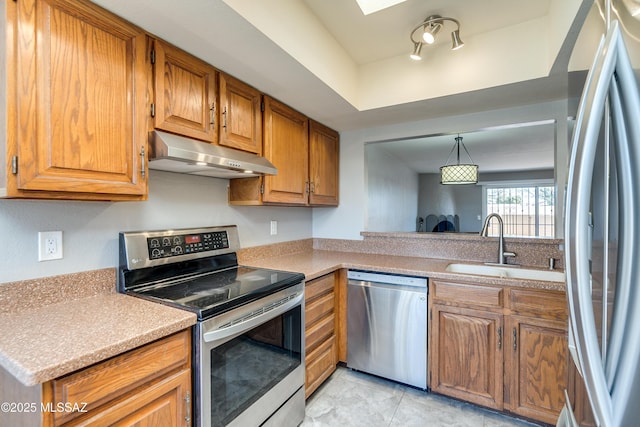 kitchen with appliances with stainless steel finishes, brown cabinets, light countertops, under cabinet range hood, and a sink