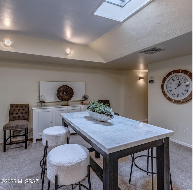 dining space featuring light carpet and vaulted ceiling with skylight