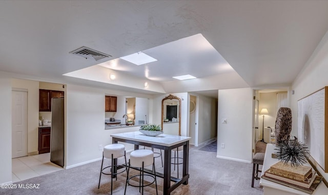 kitchen featuring sink, a breakfast bar area, a skylight, stainless steel fridge, and light colored carpet