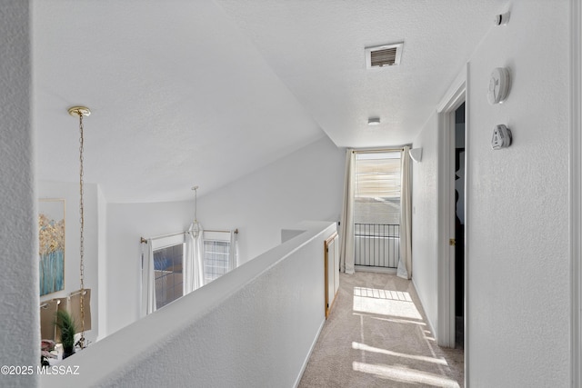 hall with light colored carpet, lofted ceiling, and a textured ceiling