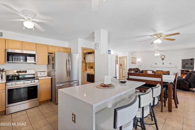 kitchen featuring light tile patterned floors, a breakfast bar area, ceiling fan, appliances with stainless steel finishes, and light brown cabinets