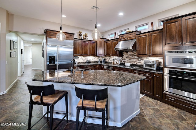 kitchen featuring dark brown cabinetry, sink, pendant lighting, stainless steel appliances, and a kitchen island with sink