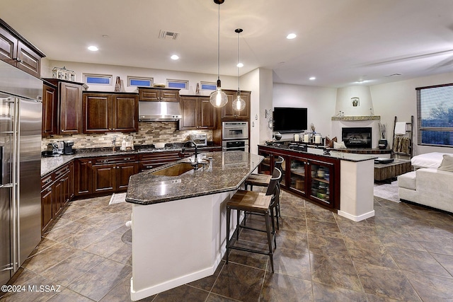 kitchen featuring pendant lighting, a kitchen island with sink, dark brown cabinetry, and appliances with stainless steel finishes