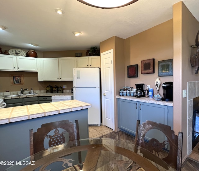 kitchen with sink, light tile patterned floors, tile counters, white appliances, and white cabinets