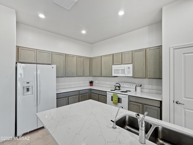 kitchen featuring a sink, visible vents, gray cabinetry, white appliances, and light stone counters