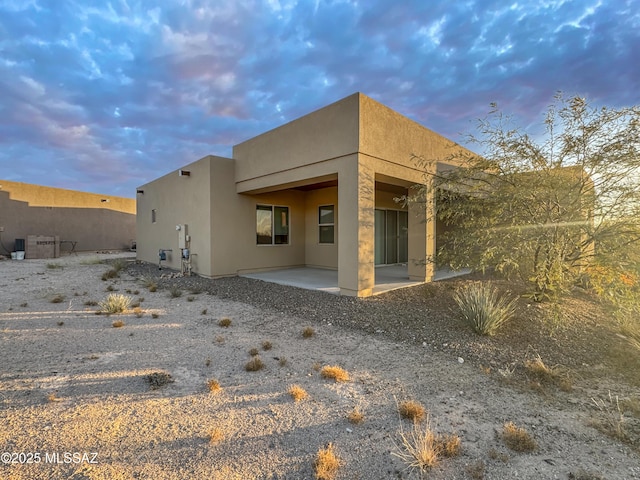 back of property at dusk with stucco siding and a patio area