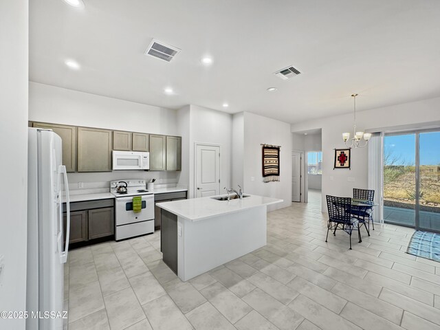 kitchen with an inviting chandelier, light countertops, visible vents, white appliances, and a kitchen island with sink