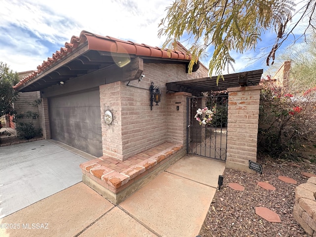 view of side of home with driveway, a gate, a tile roof, an attached garage, and brick siding