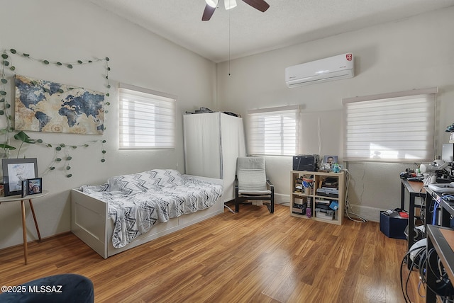 bedroom with hardwood / wood-style flooring, ceiling fan, an AC wall unit, and multiple windows