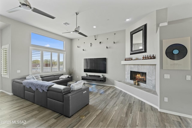 living room featuring a premium fireplace, hardwood / wood-style floors, and ceiling fan