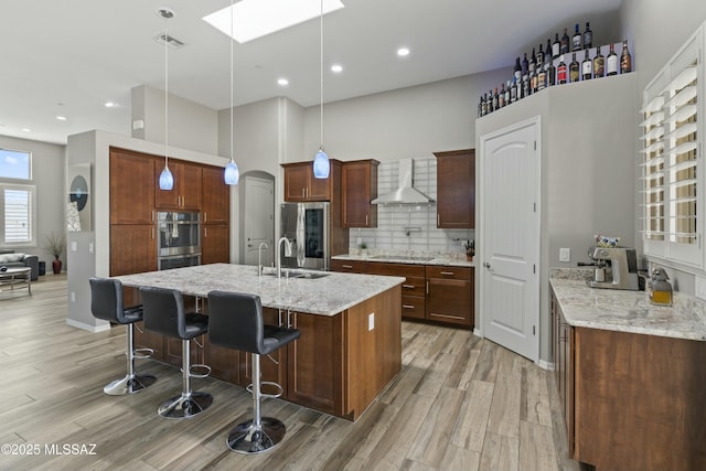 kitchen with wall chimney exhaust hood, light stone counters, a kitchen breakfast bar, pendant lighting, and stainless steel appliances