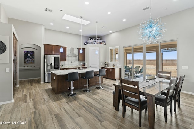 dining room with a skylight, sink, hardwood / wood-style flooring, a high ceiling, and a notable chandelier