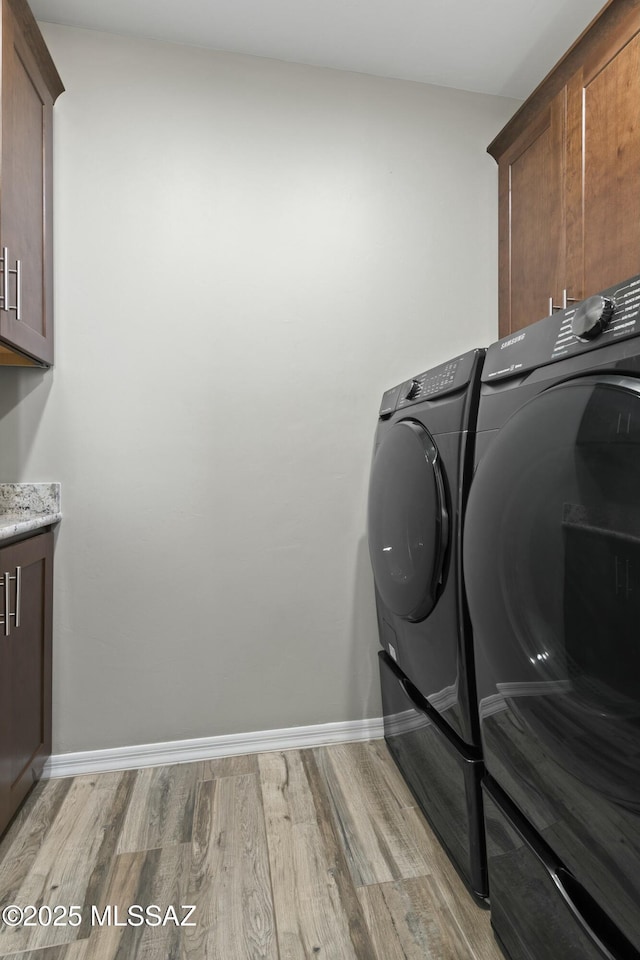 washroom featuring cabinets, washing machine and dryer, and light hardwood / wood-style flooring