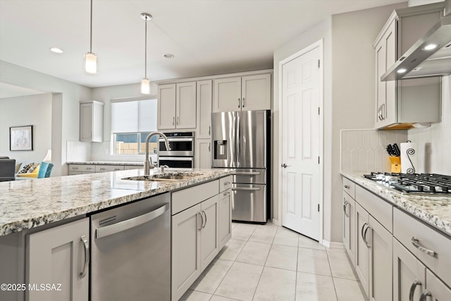 kitchen featuring appliances with stainless steel finishes, decorative light fixtures, backsplash, light stone counters, and wall chimney exhaust hood