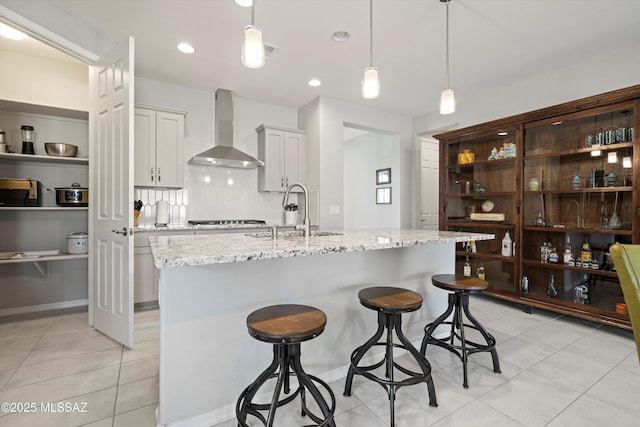 kitchen with sink, a breakfast bar area, light stone counters, decorative light fixtures, and wall chimney exhaust hood