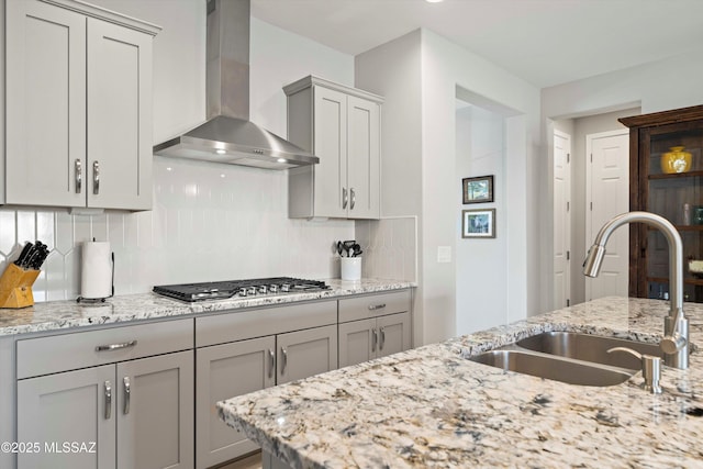 kitchen with tasteful backsplash, sink, stainless steel gas cooktop, light stone countertops, and wall chimney range hood