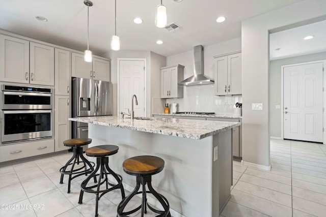 kitchen with a kitchen island with sink, sink, stainless steel appliances, and wall chimney exhaust hood