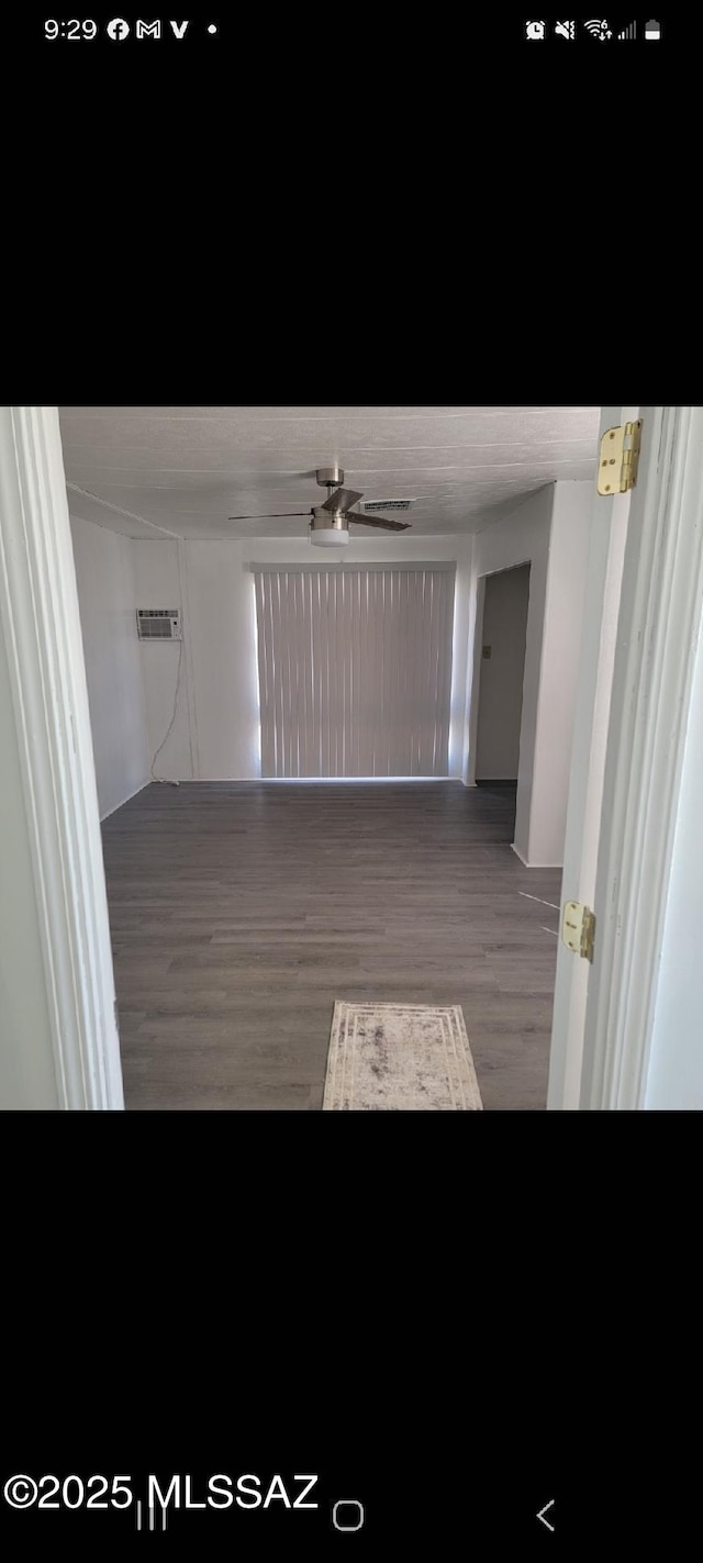 empty room with a wall unit AC, ceiling fan, and wood finished floors