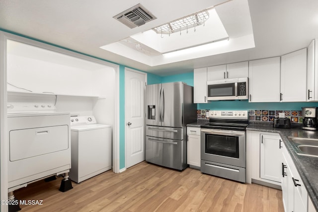 kitchen with appliances with stainless steel finishes, washer and dryer, white cabinetry, sink, and light wood-type flooring