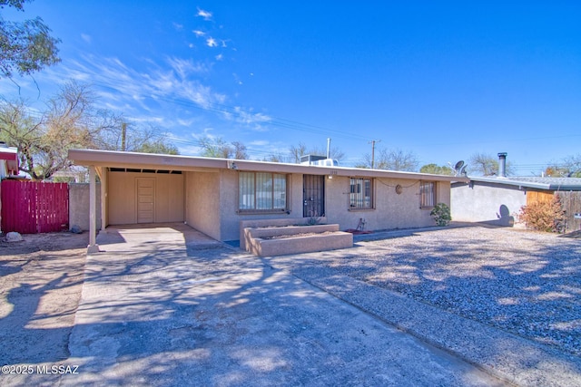 ranch-style house with an attached carport, stucco siding, fence, and driveway