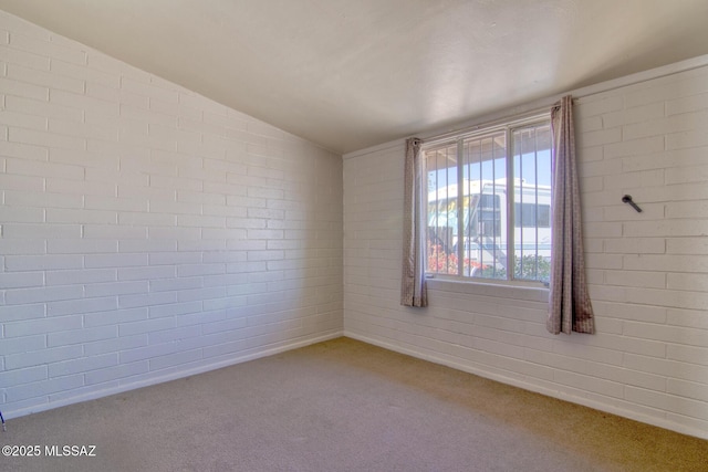 spare room with lofted ceiling, carpet flooring, and brick wall