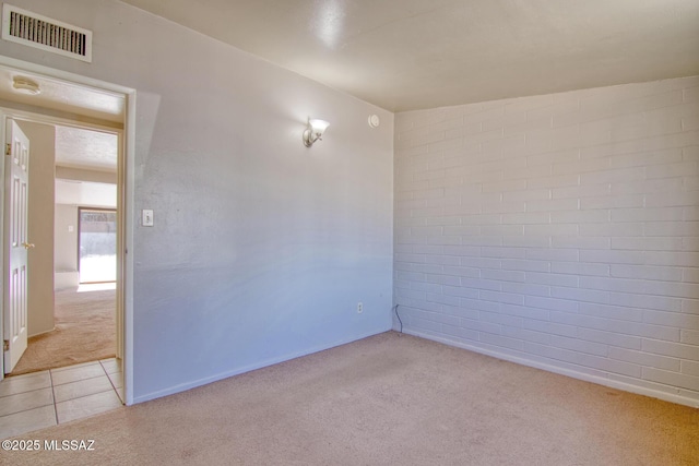 spare room featuring light tile patterned flooring, visible vents, brick wall, and light carpet