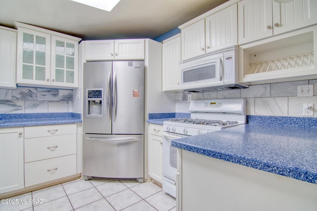 kitchen with white cabinetry, glass insert cabinets, light tile patterned floors, white appliances, and decorative backsplash