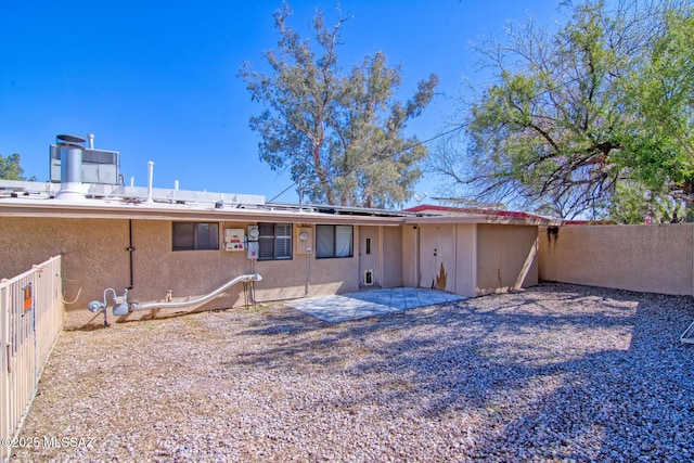 rear view of property featuring roof mounted solar panels, stucco siding, fence, and a patio area