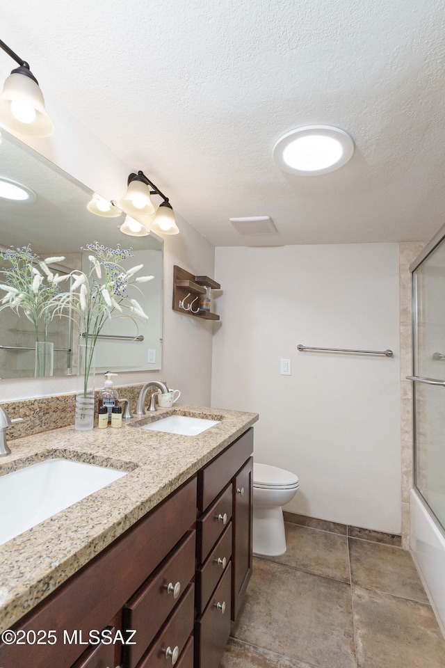 full bathroom with bath / shower combo with glass door, vanity, a textured ceiling, and toilet