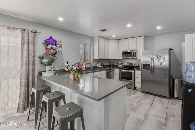 kitchen featuring sink, a breakfast bar area, kitchen peninsula, stainless steel appliances, and white cabinets