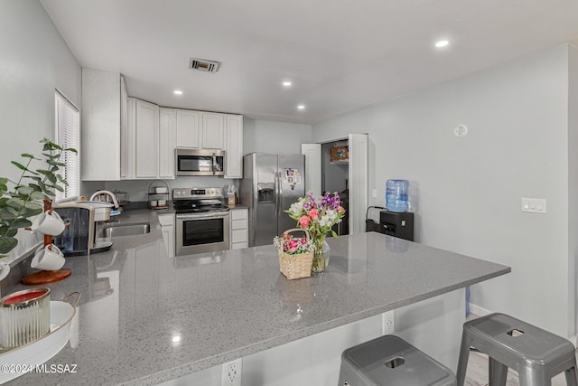 kitchen featuring sink, appliances with stainless steel finishes, light stone countertops, white cabinets, and kitchen peninsula