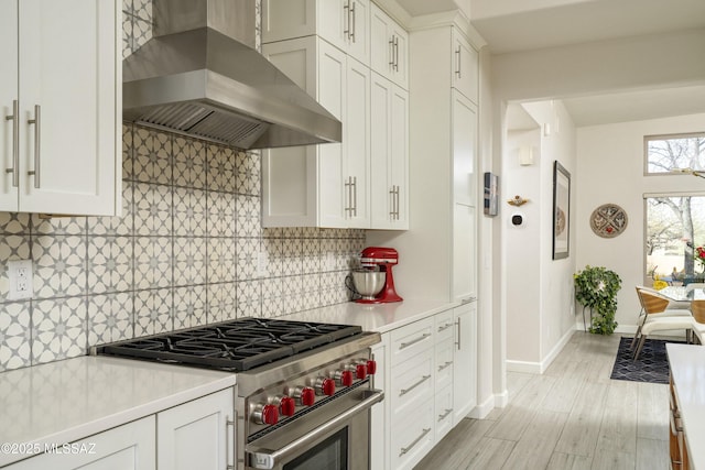 kitchen with light wood finished floors, wall chimney exhaust hood, high end stainless steel range, light countertops, and backsplash