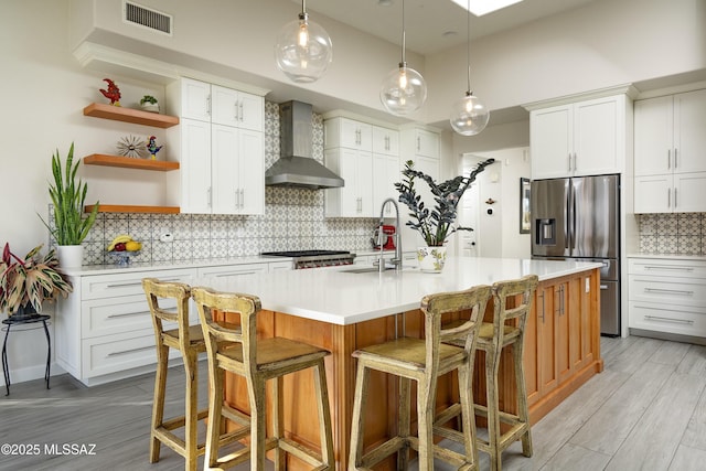 kitchen with stainless steel fridge, light countertops, wall chimney range hood, open shelves, and a sink