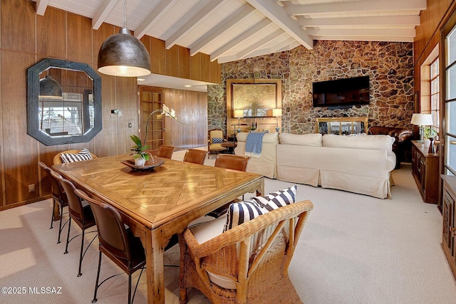 dining room with vaulted ceiling with beams, plenty of natural light, light colored carpet, and wood walls