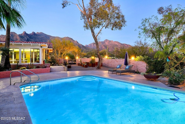 pool at dusk featuring a mountain view and a patio