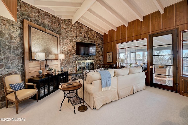 living room featuring beam ceiling, a stone fireplace, wood walls, and carpet flooring