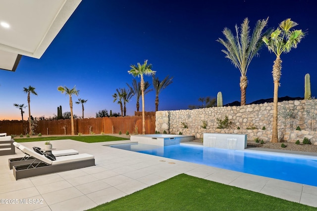 pool at dusk with an in ground hot tub and a patio area