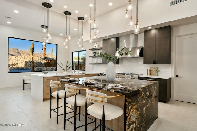 kitchen featuring backsplash, hanging light fixtures, a large island, dark brown cabinets, and wall chimney range hood