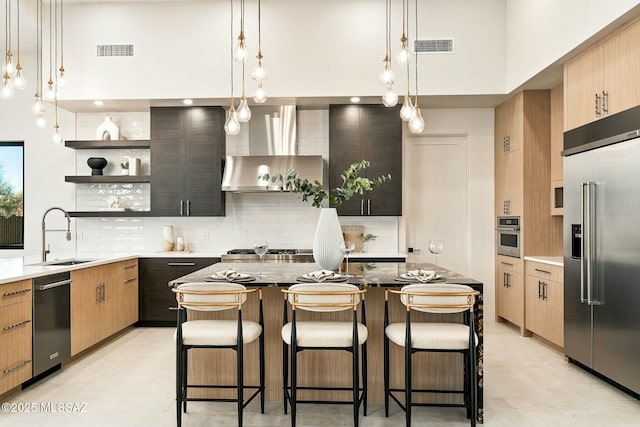 kitchen featuring wall chimney exhaust hood, appliances with stainless steel finishes, sink, and pendant lighting