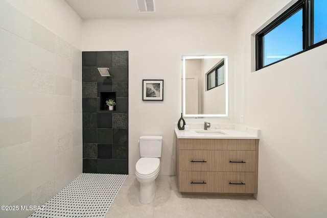 bathroom featuring vanity, a tile shower, and toilet