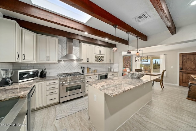 kitchen featuring wall chimney exhaust hood, stainless steel appliances, light stone counters, and a kitchen island